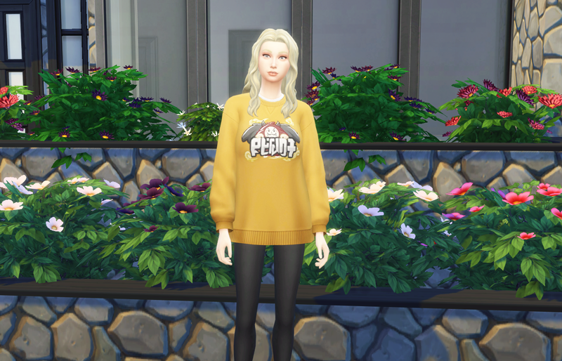 A blonde female Sim stood in front of a house with a yellow sweatshirt.